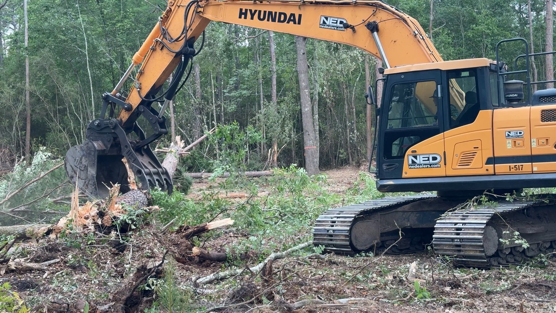 Excavator moving storm downed timber away from a driveway